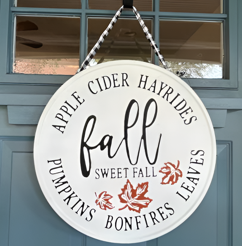 A blue front door on which a round fall board sign is attached to.